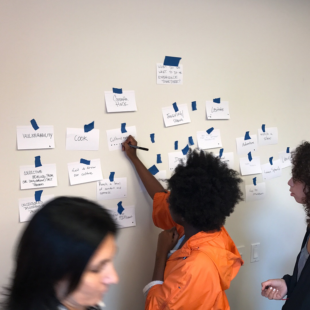 Arts Politics student in orange jacket puts up white notecard on wall with words written on them